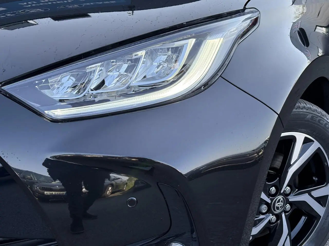 Gros plan sur l'avant droit noir intense de la Toyota Yaris 2025, mettant en valeur le phare LED et la jante alliage 16 pouces.