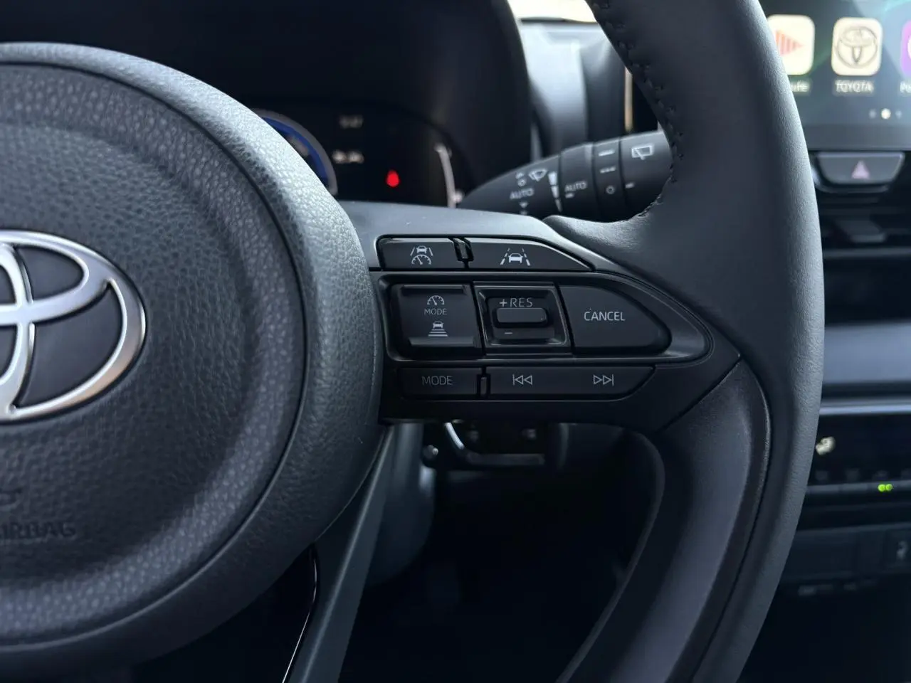 Gros plan sur le volant cuir noir de la Toyota Yaris 2025 hybride, montrant les commandes d’aide à la conduite et multimédia.