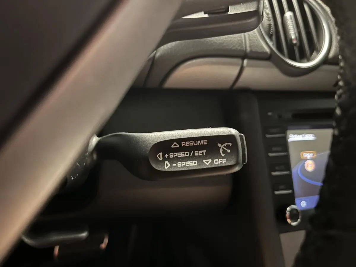 Gros plan sur la commande de régulateur de vitesse à gauche du volant dans l'habitacle noir du Porsche Cayman 987.