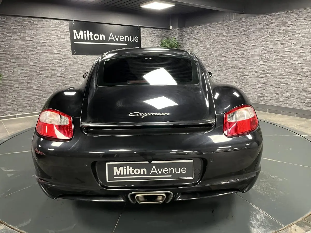 Vue arrière d'une Porsche Cayman noire 2008 avec feu arrière rouge et sortie d'échappement centrale visible.