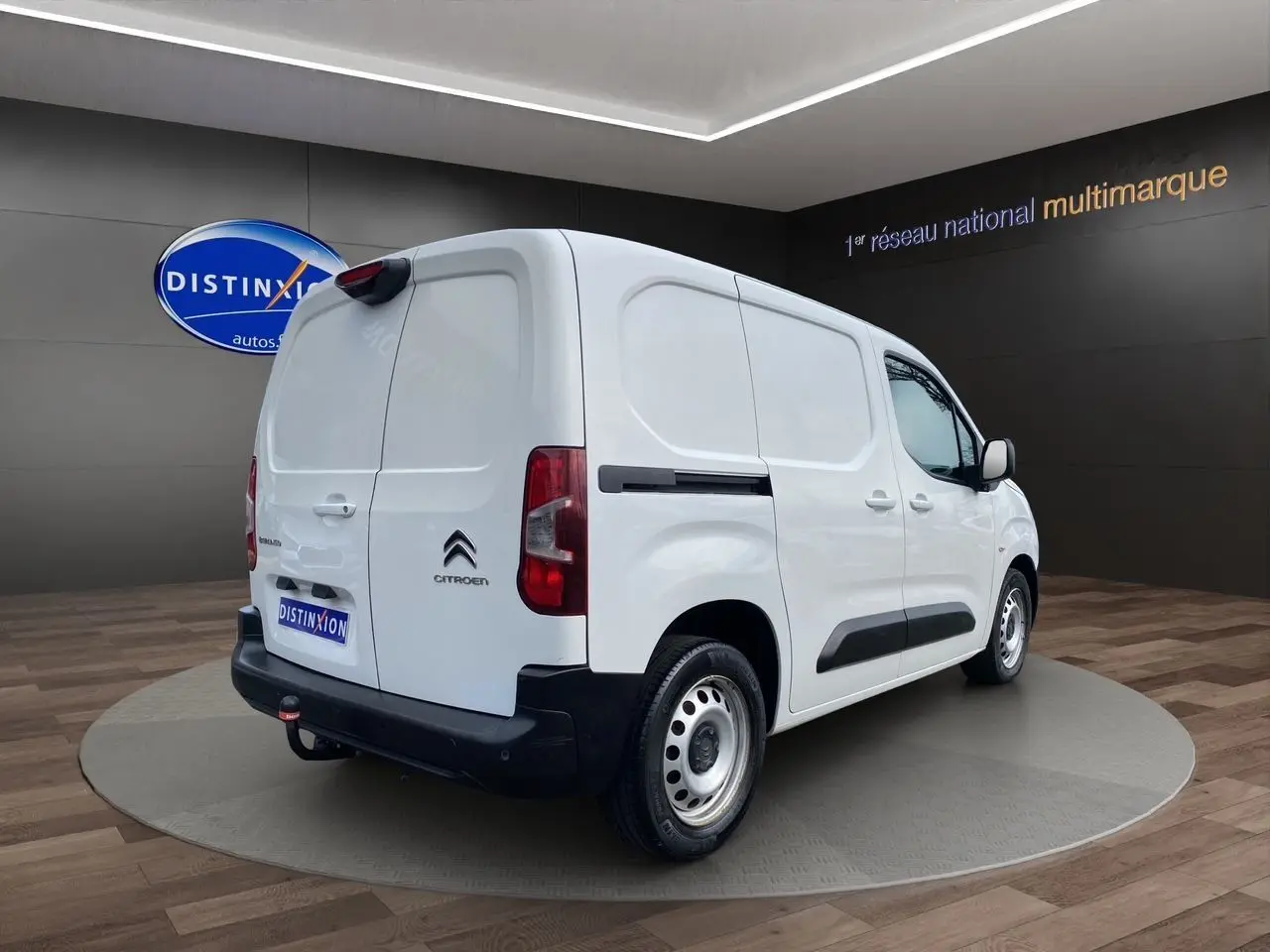 Vue 3/4 arrière droite d'un utilitaire Citroën Berlingo blanc avec hayon et pare-chocs noirs dans un showroom.