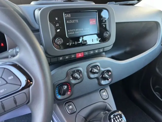 Vue intérieure du tableau de bord noir de la Fiat Panda 2025, avec écran multimédia et commandes de climatisation visibles.