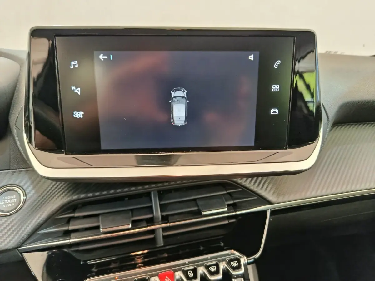Écran tactile central affichant la vue aérienne du véhicule dans l’habitacle d’une Peugeot 208 électrique blanche.