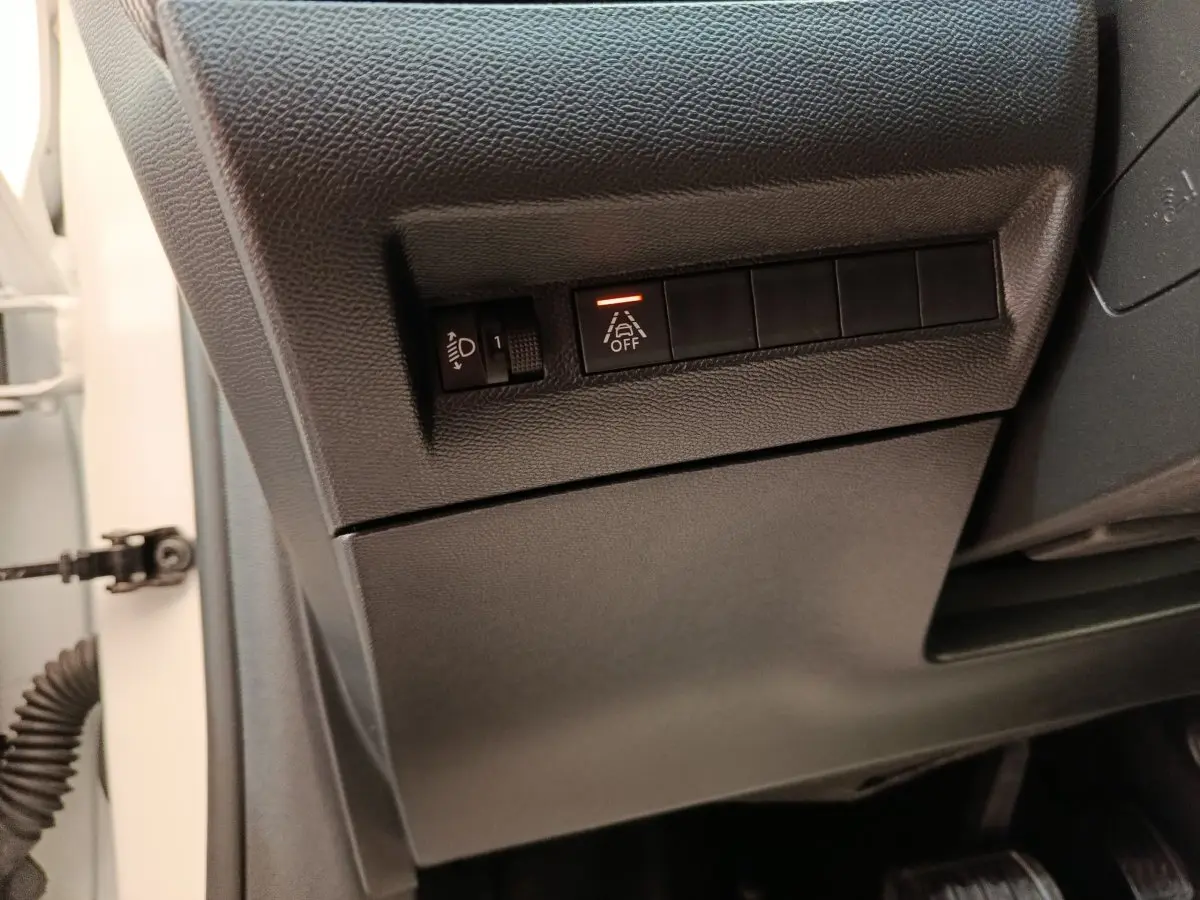 Détail intérieur côté gauche du tableau de bord noir avec commandes d’éclairage et d’aide à la conduite activée.
