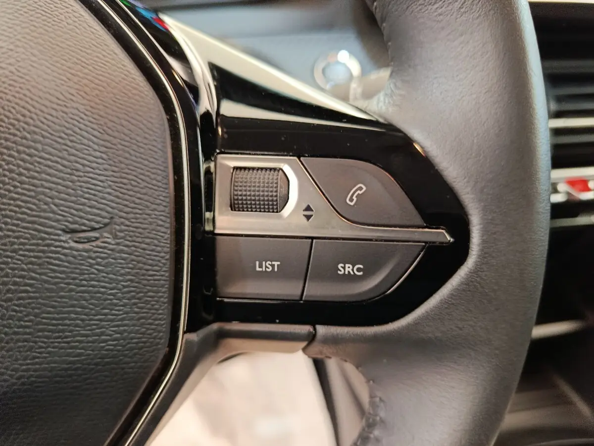 Gros plan sur les commandes gauche du volant cuir noir de la Peugeot 208 électrique blanche, boutons liste et appel.