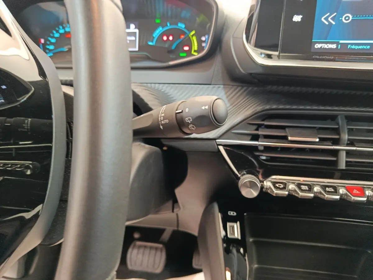 Vue intérieure rapprochée du tableau de bord et volant de la Peugeot 208 électrique, avec commandes et écran tactile visibles.