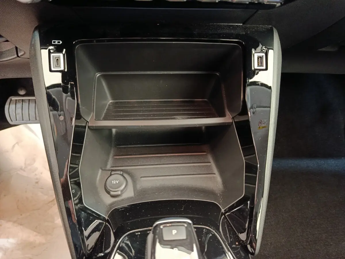 Vue plongeante sur la console centrale noire du Peugeot 208 électrique 2021 avec prise 12V et ports USB.