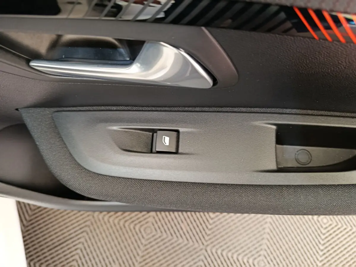 Détail de la commande de lève-vitre et poignée intérieure sur la porte côté conducteur d'une Peugeot 208 blanche électrique.
