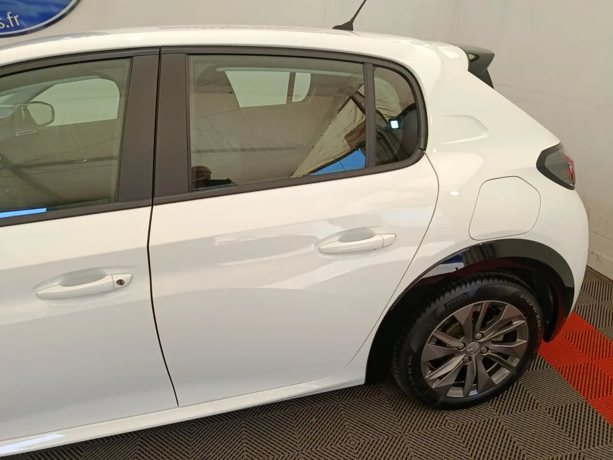 Vue latérale droite sur la partie arrière d’une Peugeot 208 électrique blanche avec jante alliage et porte de recharge visible.
