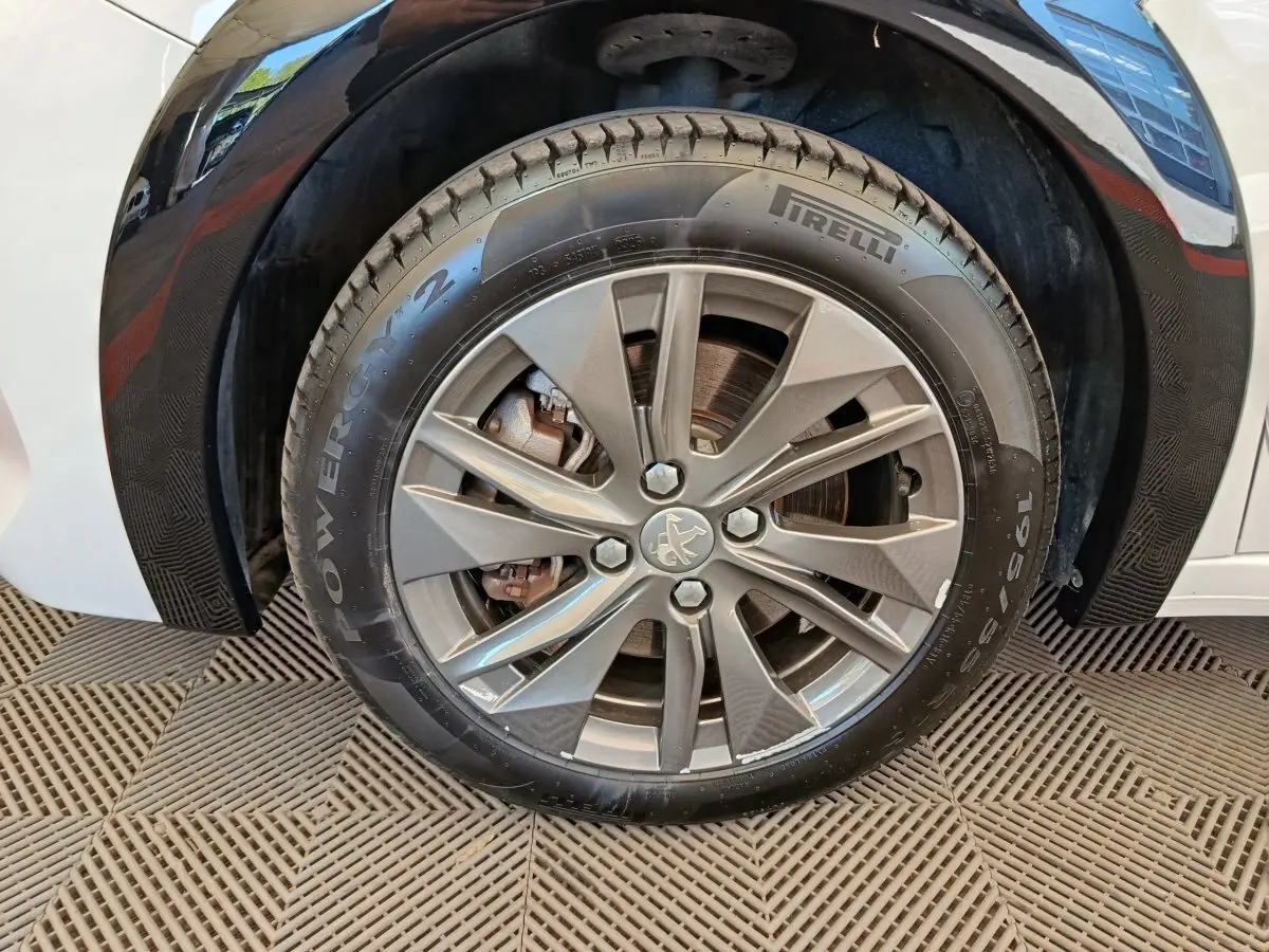 Gros plan sur la roue avant droite d'une Peugeot 208 électrique blanche, avec jante alliage et pneu Pirelli.