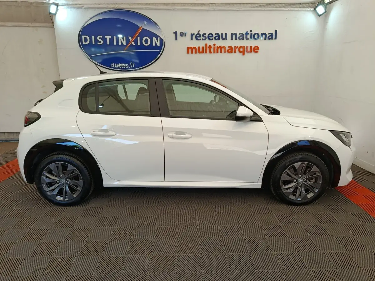 Profil côté gauche d'une Peugeot 208 électrique Active Business R blanche, vue en intérieur sur fond neutre.