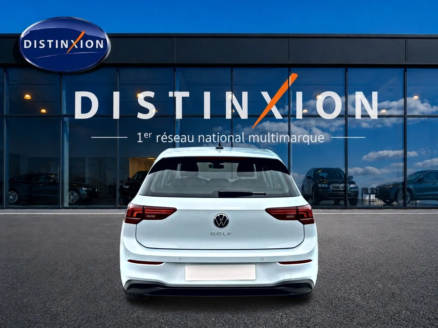 Vue arrière d'une Volkswagen Golf blanche garée devant une vitrine avec logo Distinxion.
