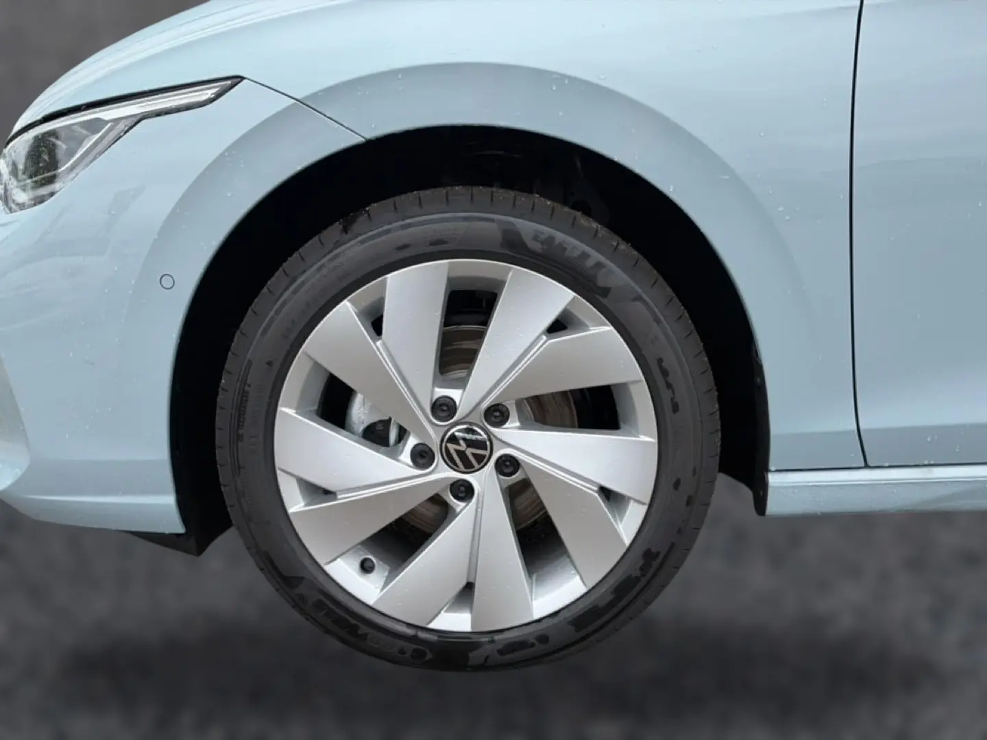 Gros plan sur la roue avant gauche d’une Volkswagen Golf bleu glacier avec jante alu 17 pouces au design moderne.