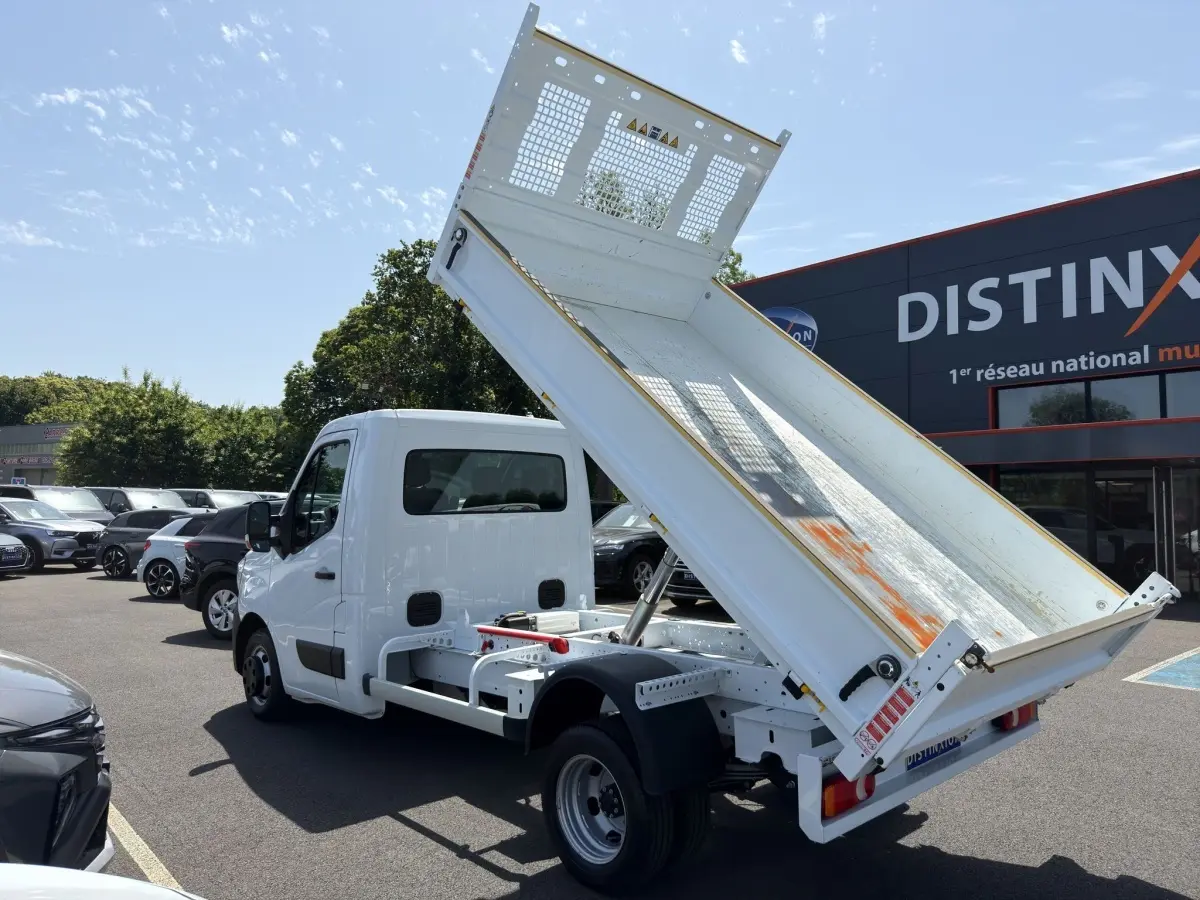 Renault Master blanc vue 3/4 arrière avec benne relevée sur parking ensoleillé.