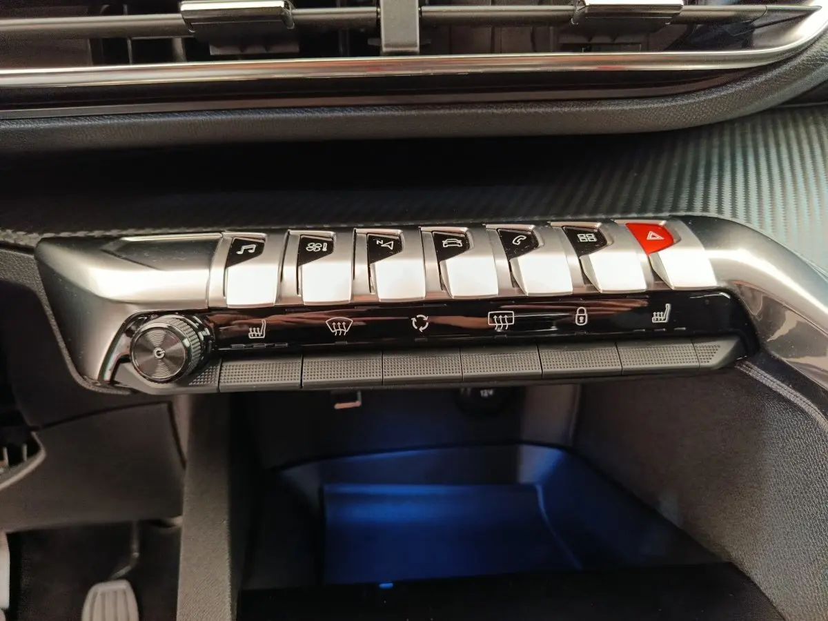 Gros plan sur la rangée de boutons métalliques et commandes de climatisation du tableau de bord du Peugeot 3008 gris foncé.