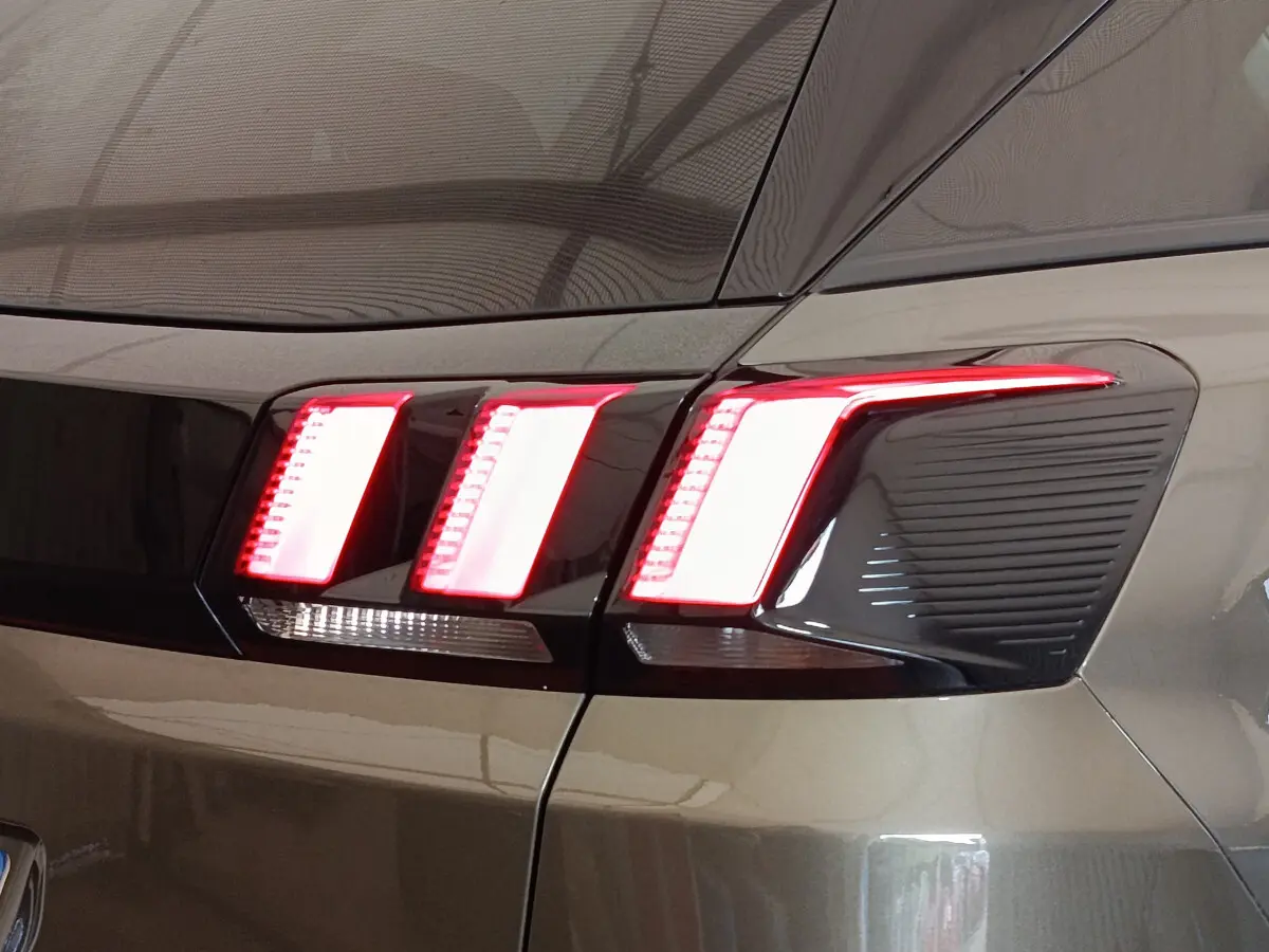 Gros plan sur les feux arrière allumés du Peugeot 3008 gris foncé, côté gauche, soulignant son design moderne.