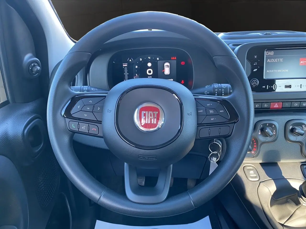 Vue rapprochée du volant noir FIAT Panda 2025 avec commandes intégrées et tableau de bord numérique allumé.