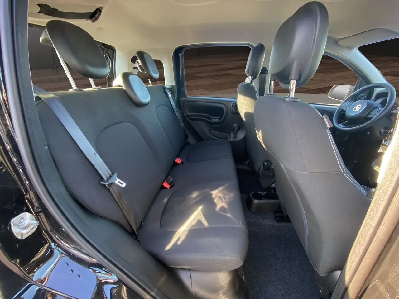 Intérieur arrière de la Fiat Panda noire 2025, vue côté gauche montrant les sièges en tissu noir et ceintures de sécurité.