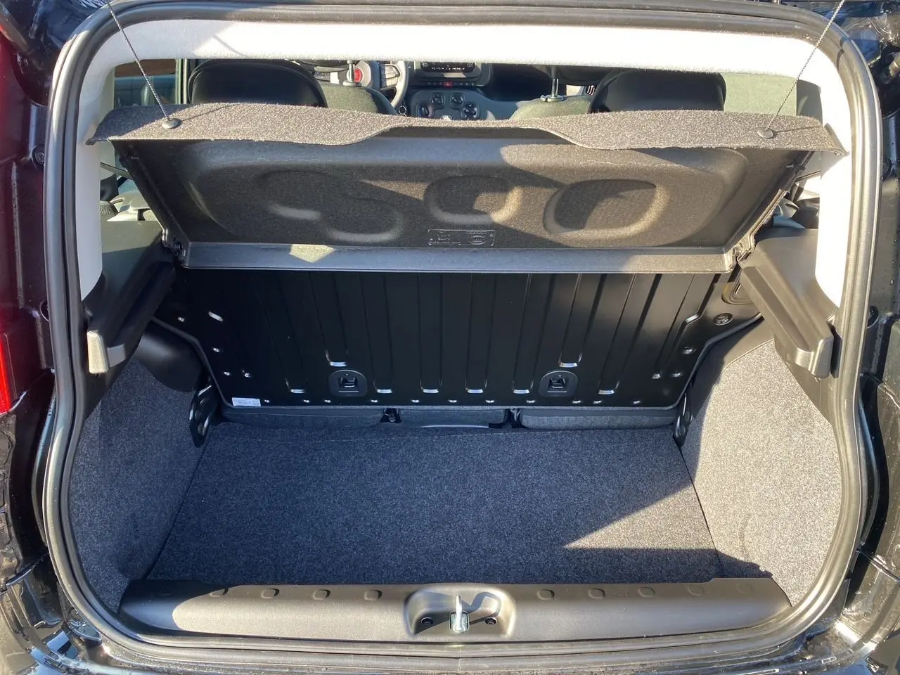 Coffre ouvert vu de l'arrière d'une FIAT Panda noire 2025, montrant l'espace de chargement et l'intérieur arrière.