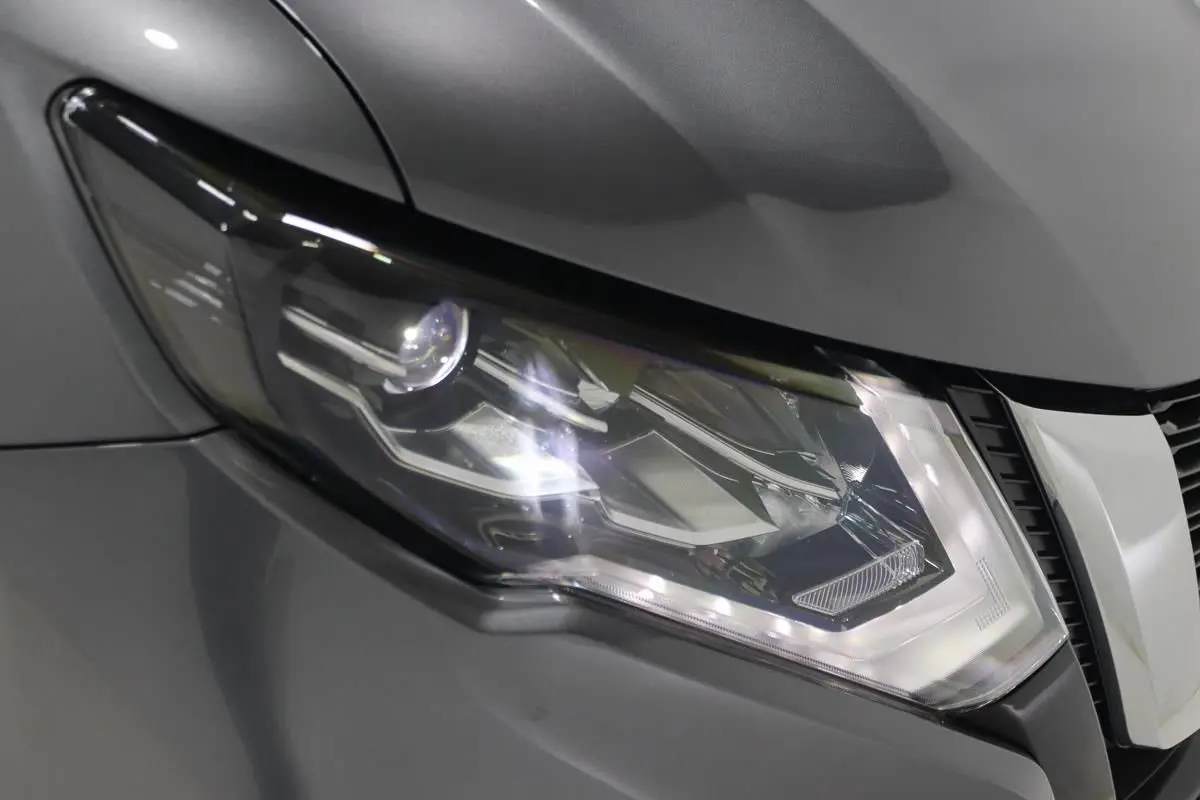 Gros plan sur le phare avant droit du Nissan X-TRAIL gris métallisé, soulignant ses lignes modernes et LED.
