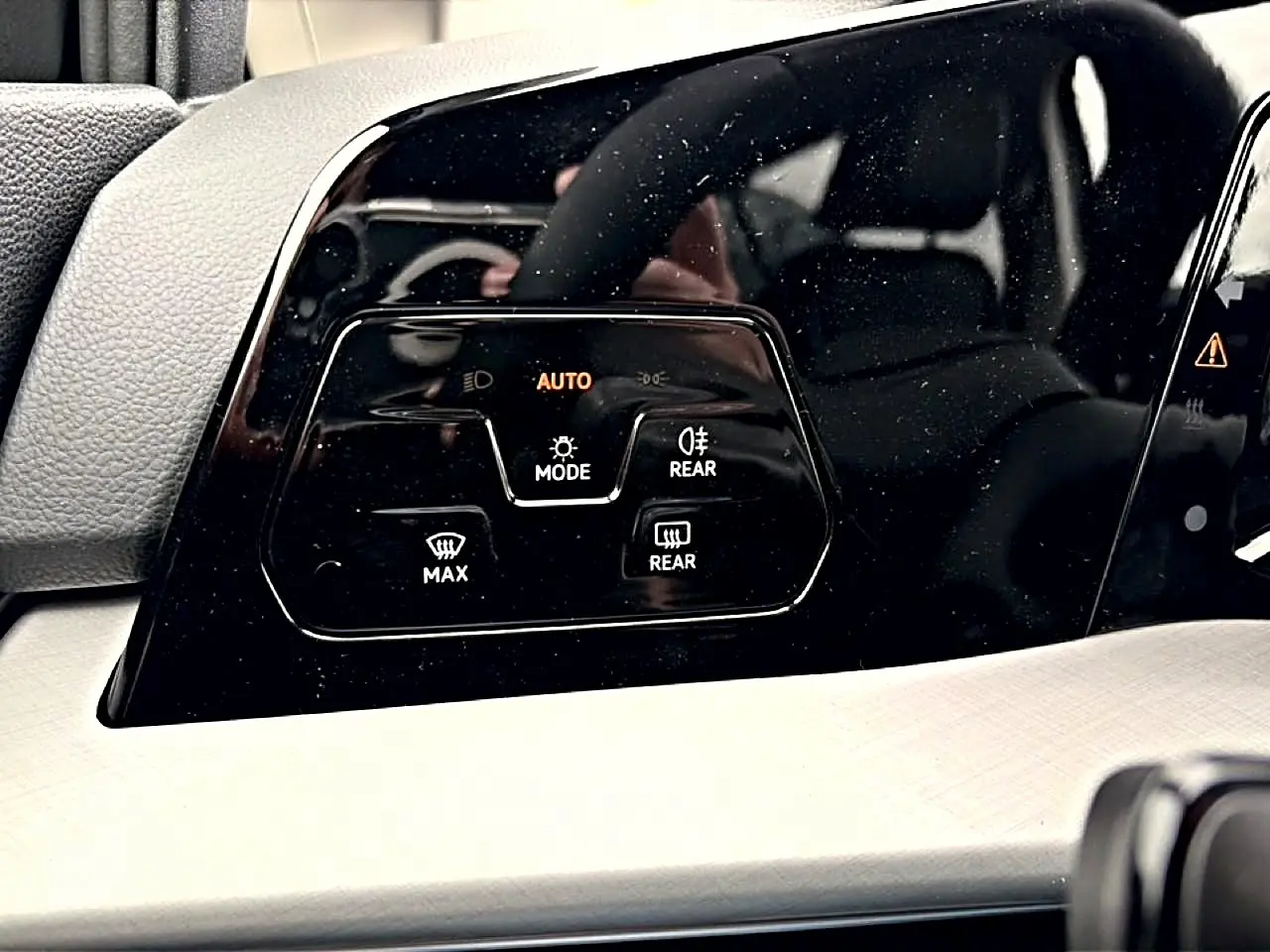Gros plan sur les commandes de phares automatiques et de désembuage du tableau de bord noir de la Volkswagen Golf 2026.