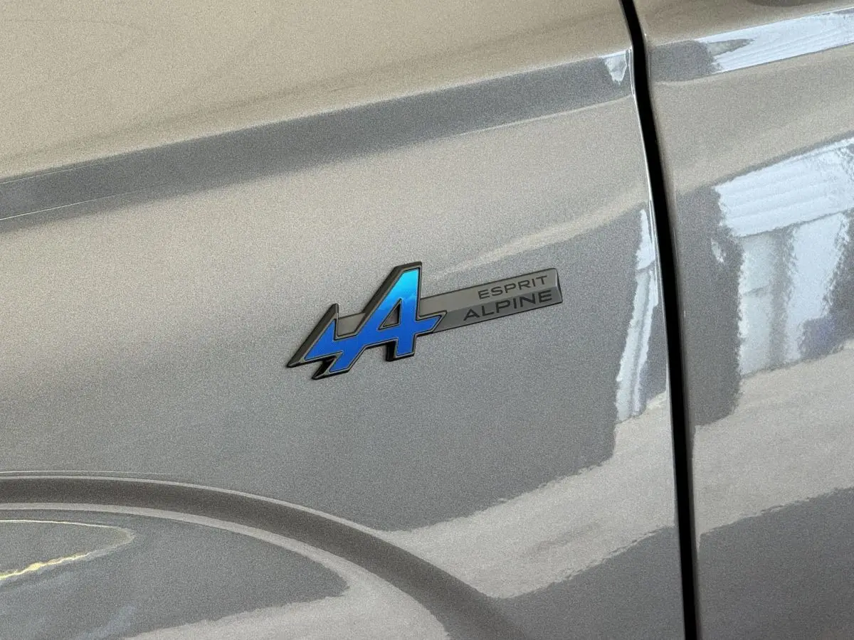 Gros plan sur l'écusson bleu "Esprit Alpine" sur la porte gris foncé d'un Renault Espace hybride 2025.