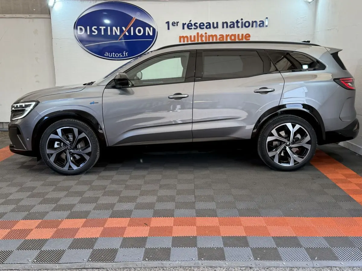 Profil côté gauche d'un Renault Espace esprit Alpine gris foncé, hybride essence, roues alliage et logo Distinxion en arrière-plan.