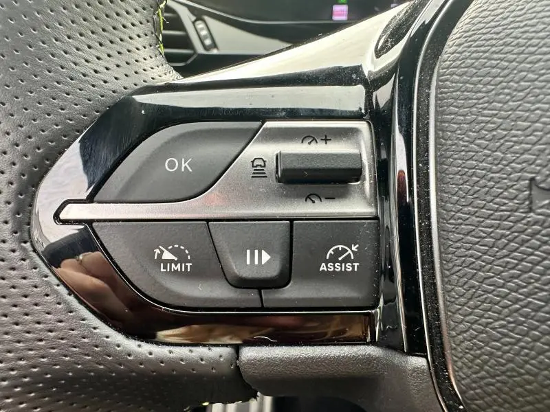 Gros plan sur les commandes noires du volant multifonction à gauche de la Peugeot 308 SW 2023, finition brillante.