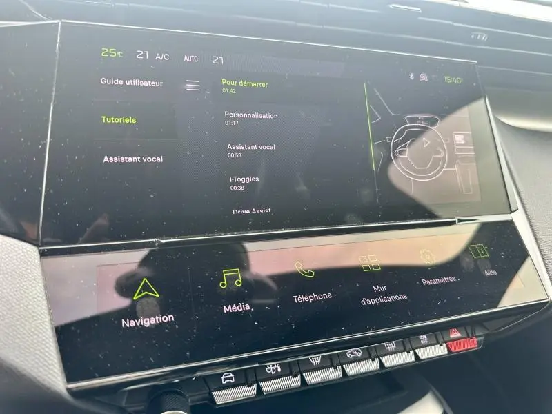 Écran tactile central du tableau de bord de la Peugeot 308 SW 2023 affichant le menu tutoriels et assistant vocal.
