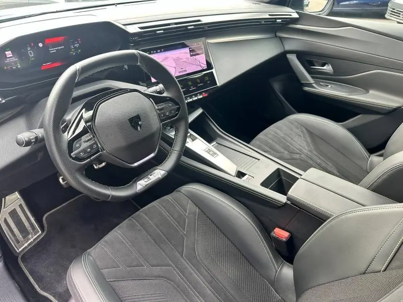 Intérieur noir de la Peugeot 308 SW 2023, vue côté conducteur sur le tableau de bord et volant multifonction moderne.
