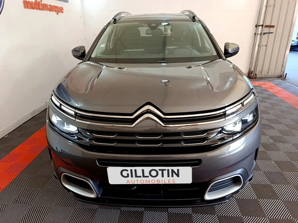 Vue avant d'un Citroën C5 Aircross gris foncé avec feux LED allumés et calandre chromée en intérieur showroom.