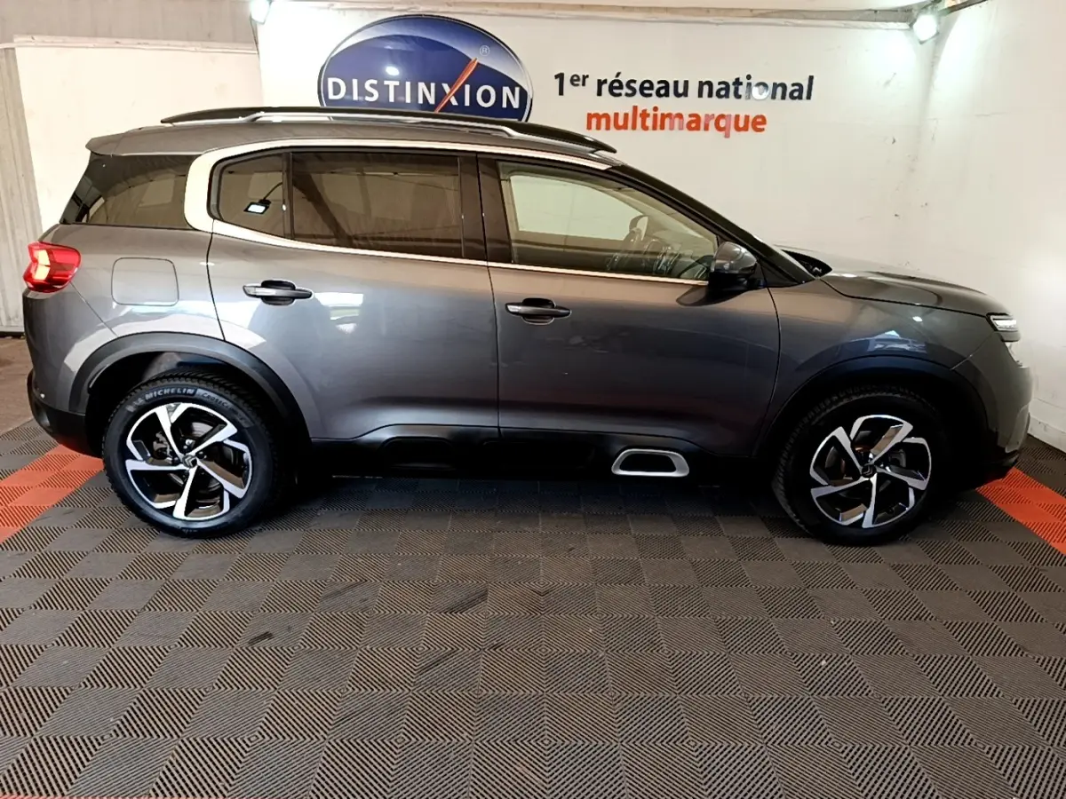 Vue de profil côté gauche d'un Citroën C5 Aircross gris foncé avec jantes alliage et barres de toit chromées.