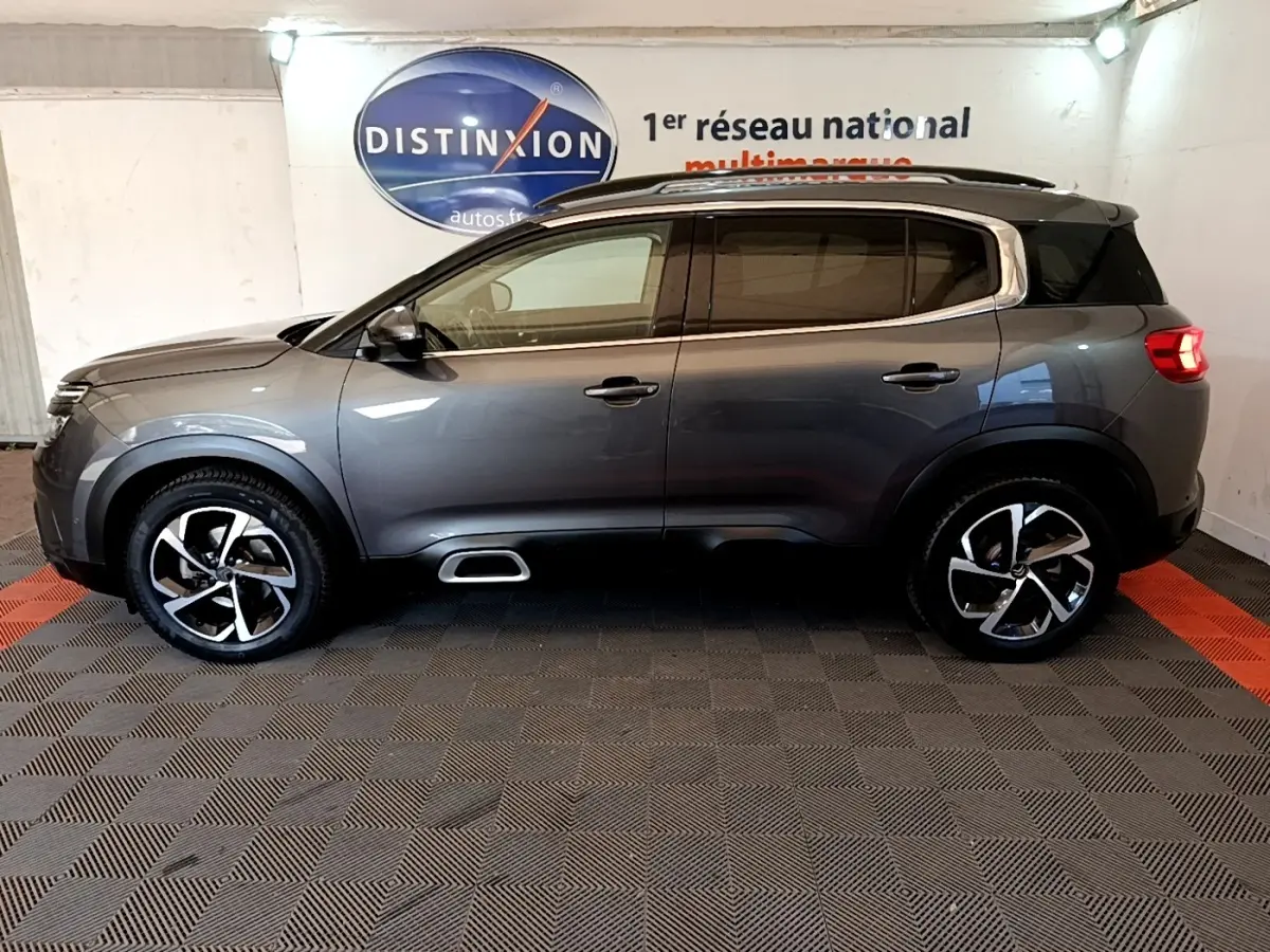 Profil côté gauche d'un Citroën C5 Aircross gris foncé 2020 avec jantes alliage et barres de toit chromées.