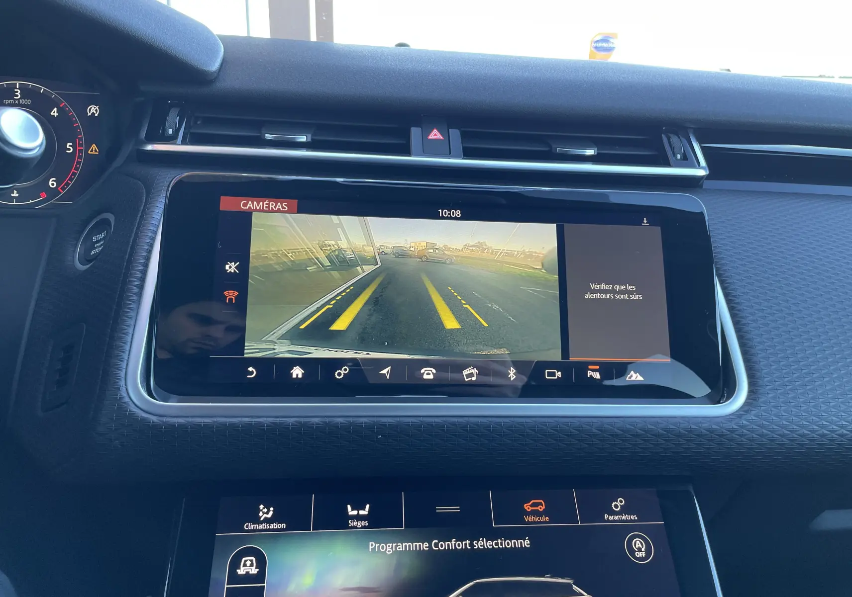 Vue rapprochée de l'écran central du Range Rover Velar gris, affichant la caméra de recul avec lignes de guidage jaunes.