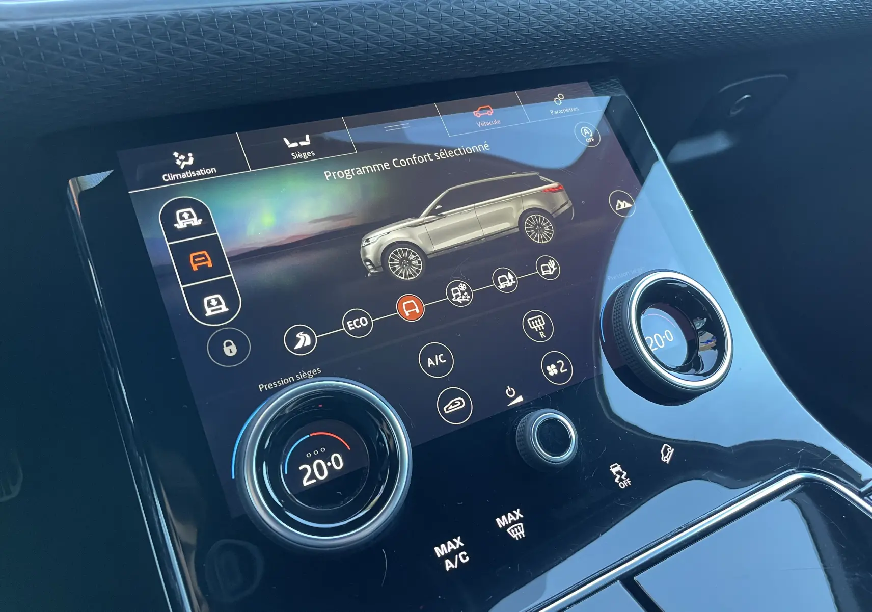 Écran tactile central du Range Rover Velar gris, affichant le programme confort avec réglages climatisation et sièges.
