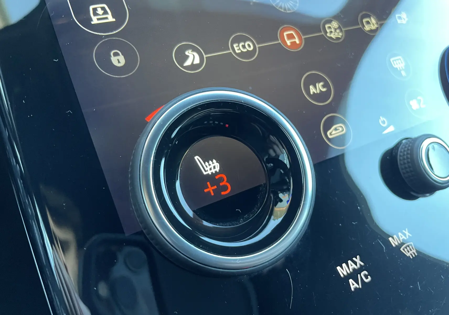 Gros plan sur le bouton de réglage du siège chauffant à +3 du Range Rover Velar gris dans la console centrale.