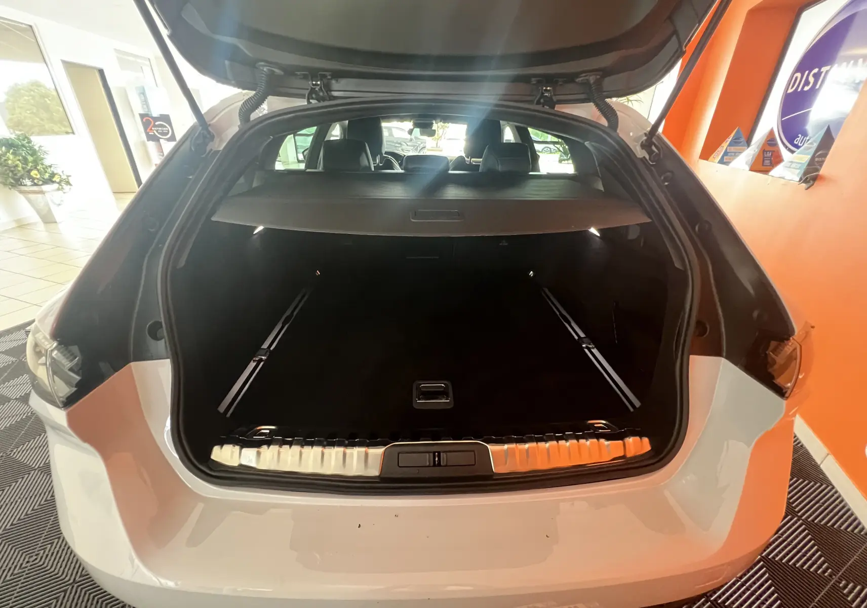Coffre ouvert vu de l'arrière d'une Peugeot 508 SW blanche 2024, montrant l'espace de chargement et la plage arrière.