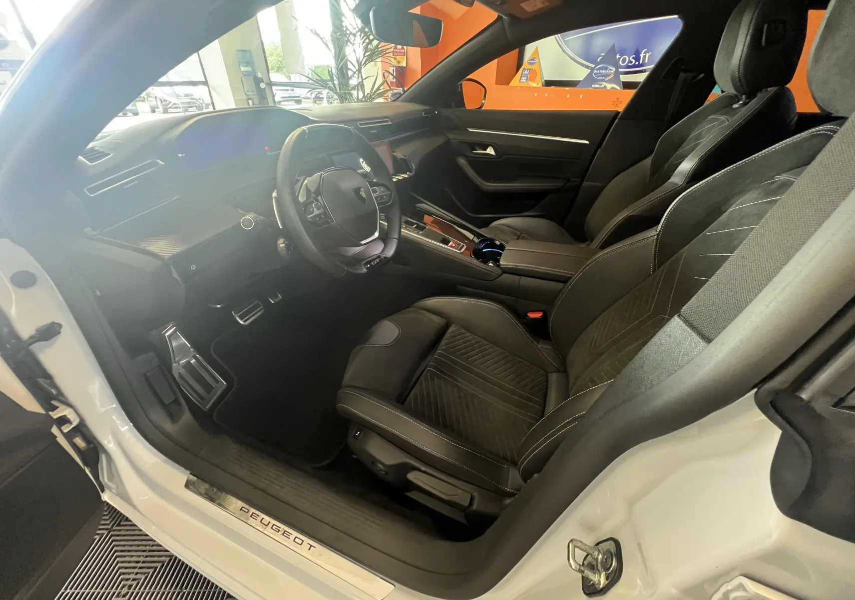 Intérieur côté conducteur d'une Peugeot 508 SW blanche 2024, sièges en cuir noir et tableau de bord moderne.