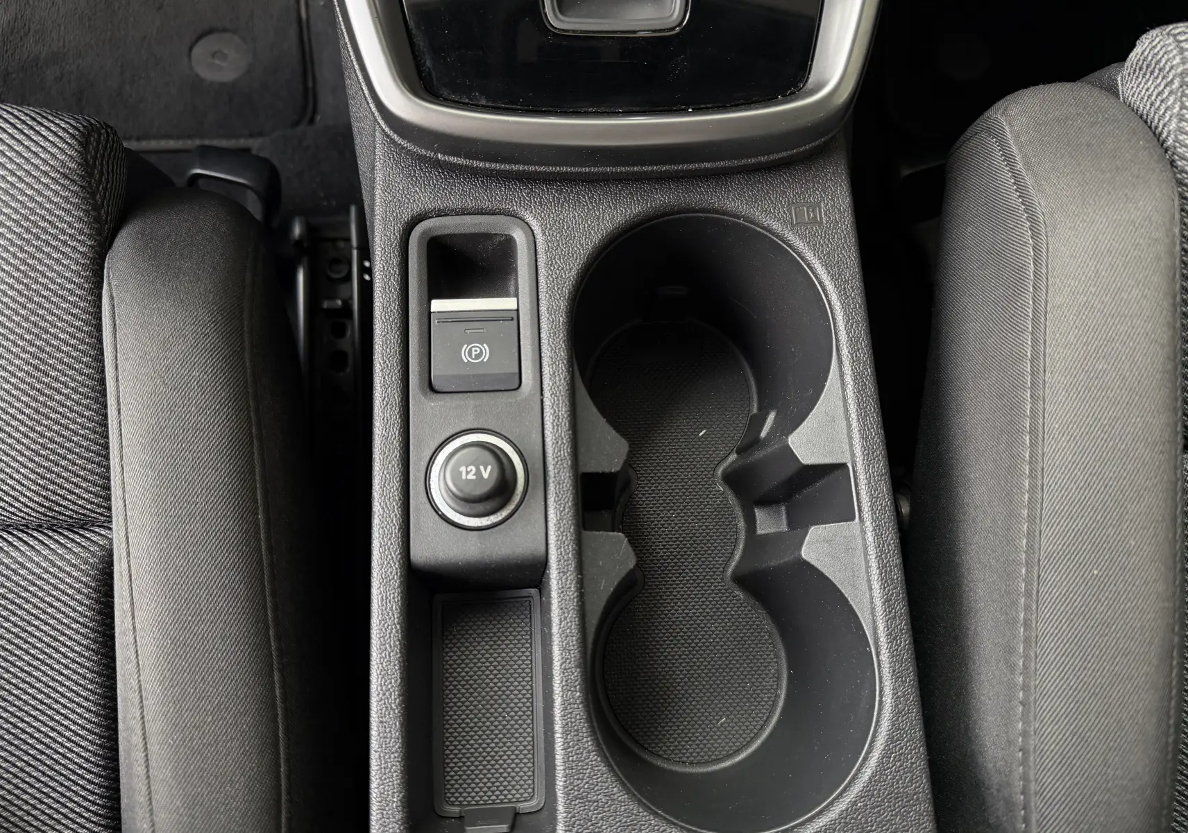 Vue plongeante sur la console centrale noire de l'Audi A3 Sportback, avec porte-gobelets et prise 12V visible entre les sièges avant.