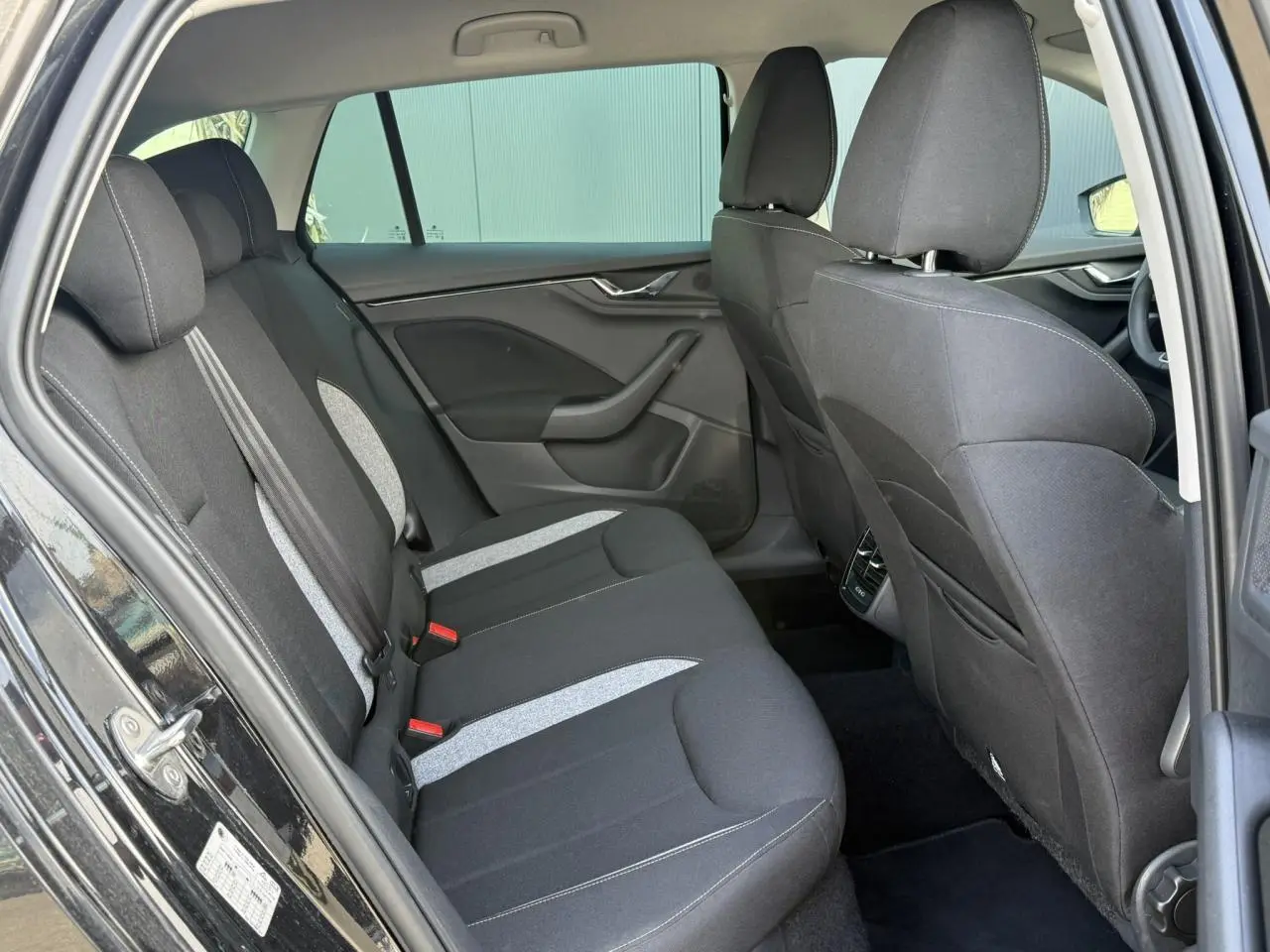 Vue côté gauche de l'habitacle arrière d'une Skoda Scala noir Magic Perle avec sièges tissu bicolores et surpiqûres claires.