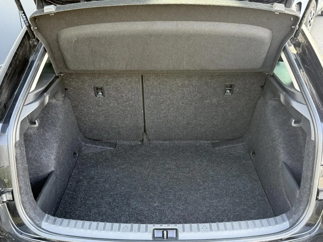 Coffre ouvert vu de l'arrière d'une Skoda Scala TSI 116 DSG7 noir Magic Perle, intérieur en moquette grise.