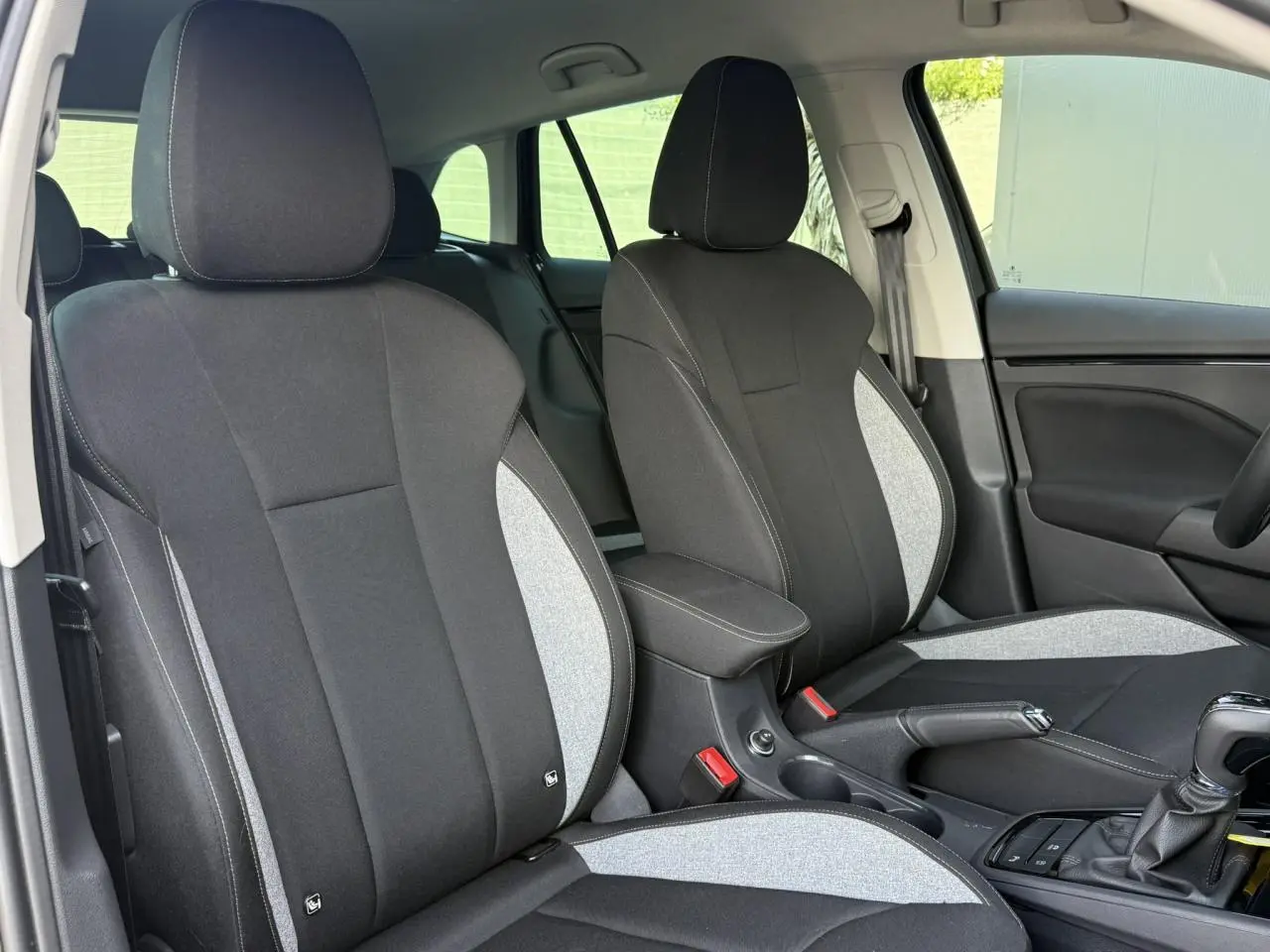 Vue intérieure des sièges avant bi-ton gris et noir de la Skoda Scala TSI 116 DSG7 avec accoudoir central et levier de vitesse.