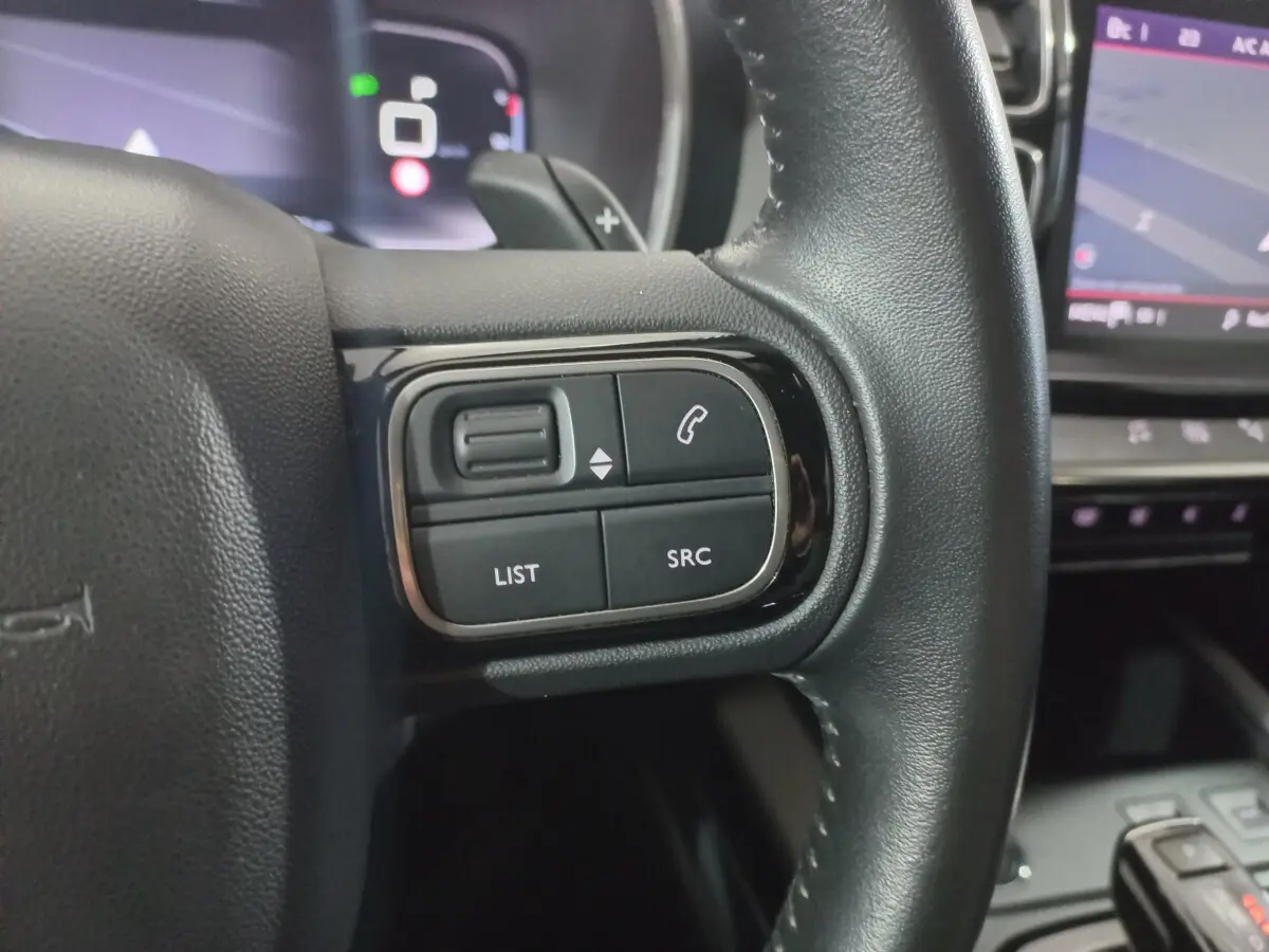 Gros plan sur les commandes gauche du volant cuir noir d'une Citroën C5 Aircross 2020 avec écran tactile en arrière-plan.