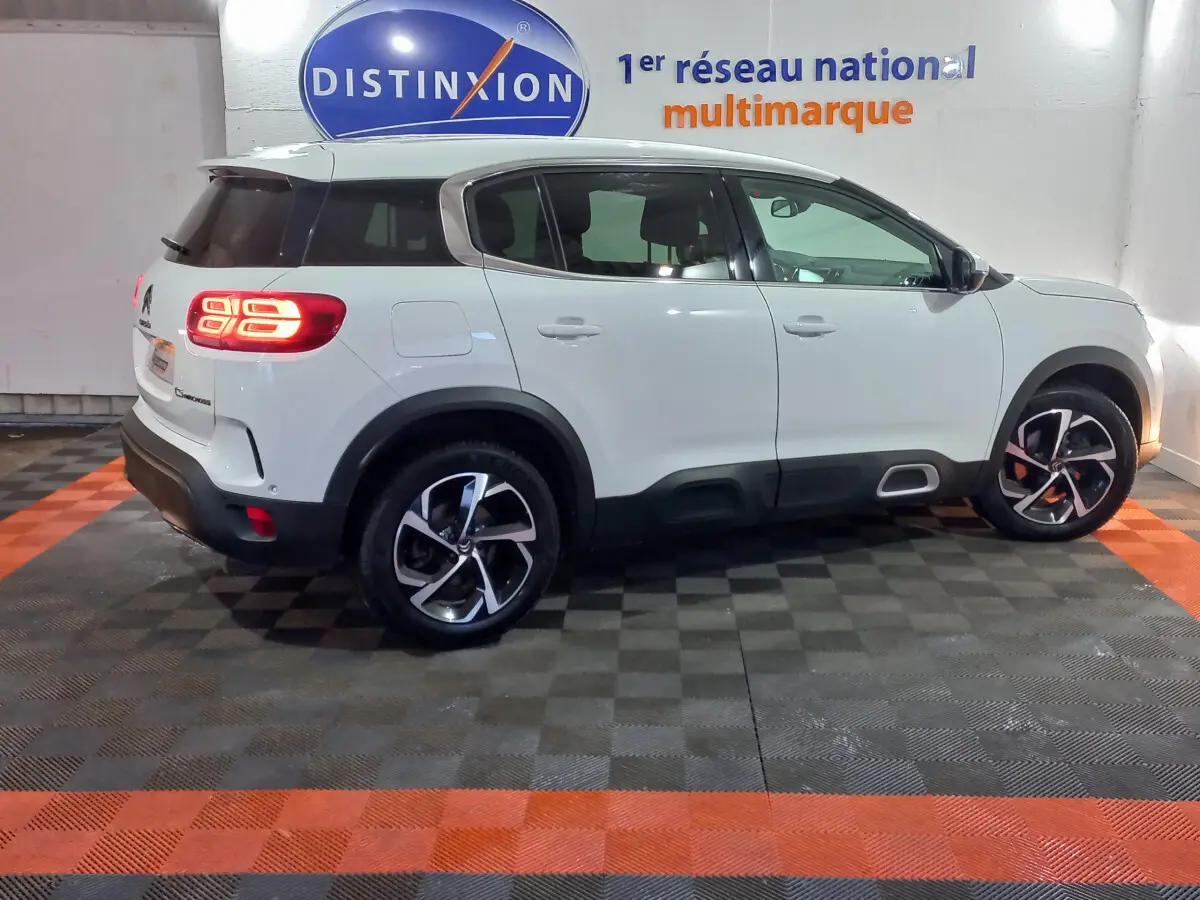 Vue de profil côté gauche d'un Citroën C5 Aircross blanc avec feux arrière allumés dans un showroom.