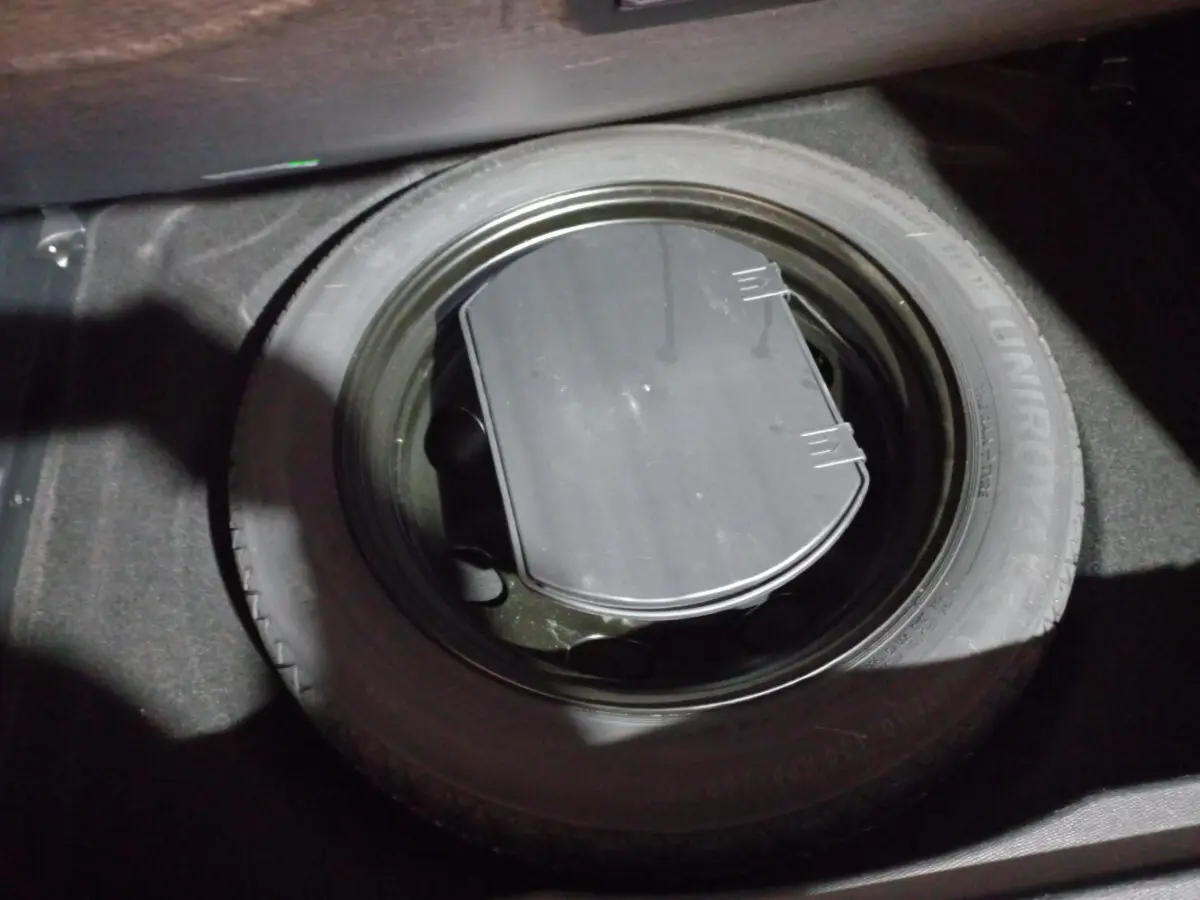 Gros plan sur la roue de secours noire dans le coffre d'un Citroën C5 Aircross blanc, vue intérieure depuis le dessus.