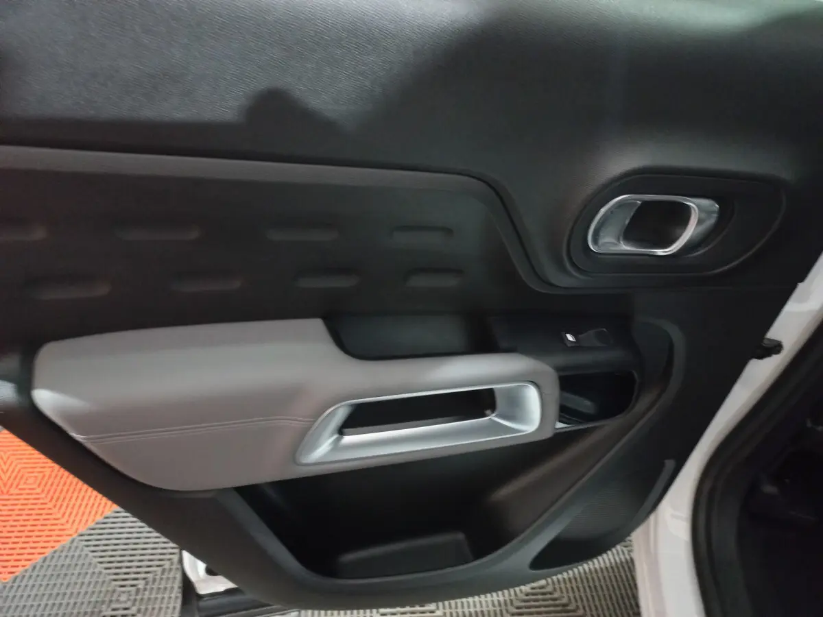 Gros plan sur la porte intérieure côté droit du Citroën C5 Aircross blanc, avec poignée argentée et garniture noire et grise.