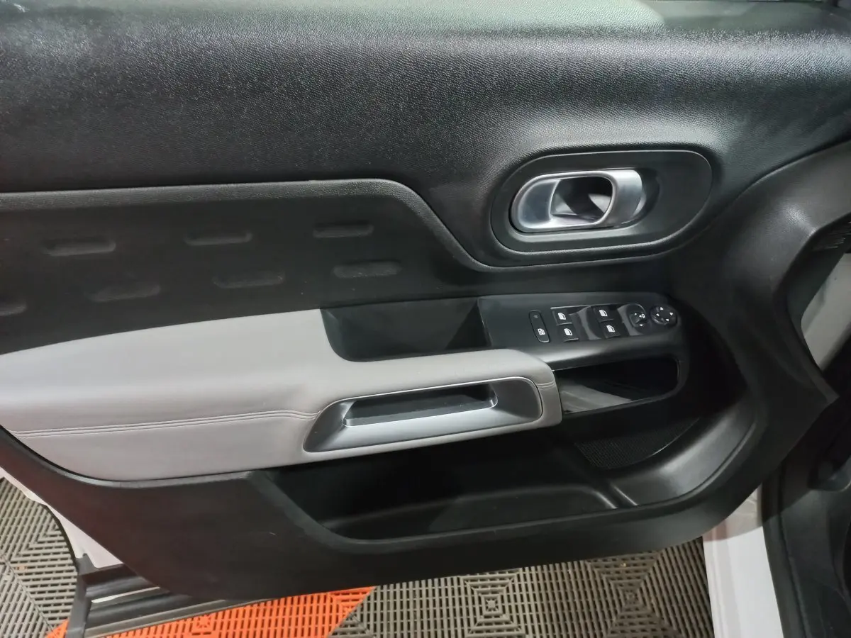 Gros plan sur la porte avant droite intérieure du Citroën C5 Aircross blanc, avec commandes électriques et poignée argentée.