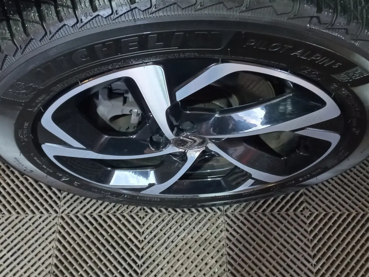 Gros plan sur la jante noire et argentée d'un Citroën C5 Aircross blanc, mettant en valeur le logo central et le pneu Michelin.