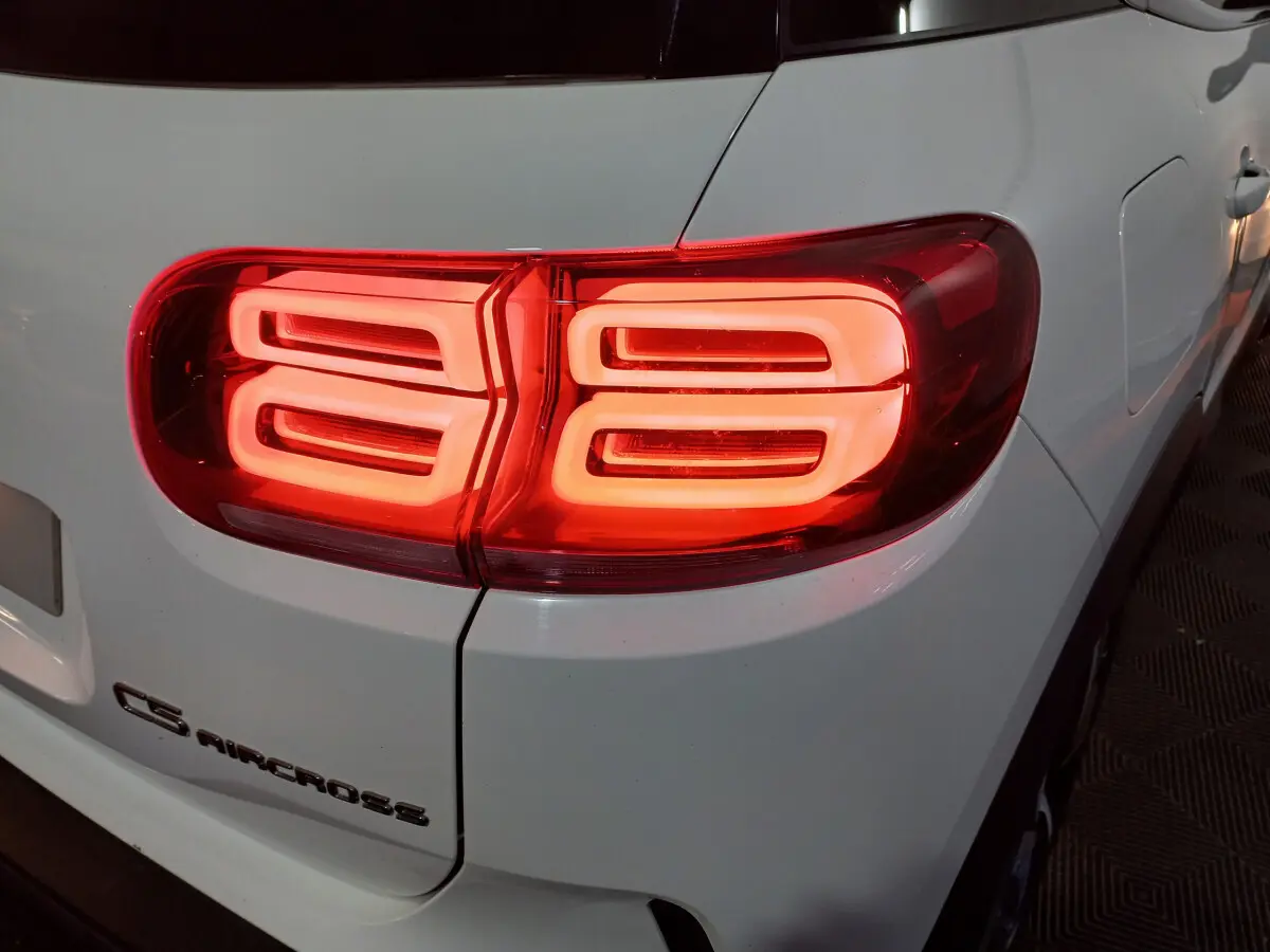 Gros plan sur le feu arrière droit rouge allumé d'un Citroën C5 Aircross blanc, avec logo visible sur la carrosserie.