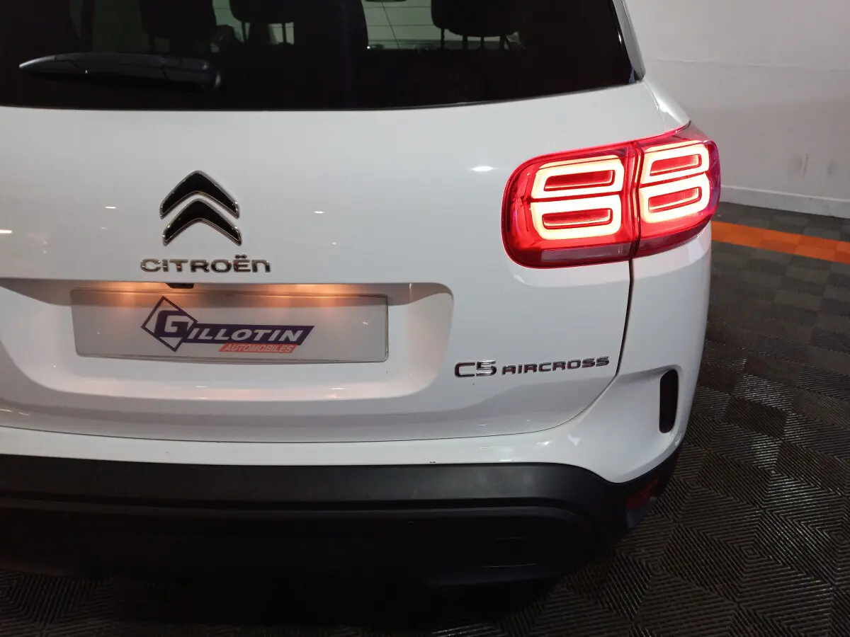 Vue arrière droite d'un Citroën C5 Aircross blanc avec feux arrière allumés et logo visible sur un sol carrelé.